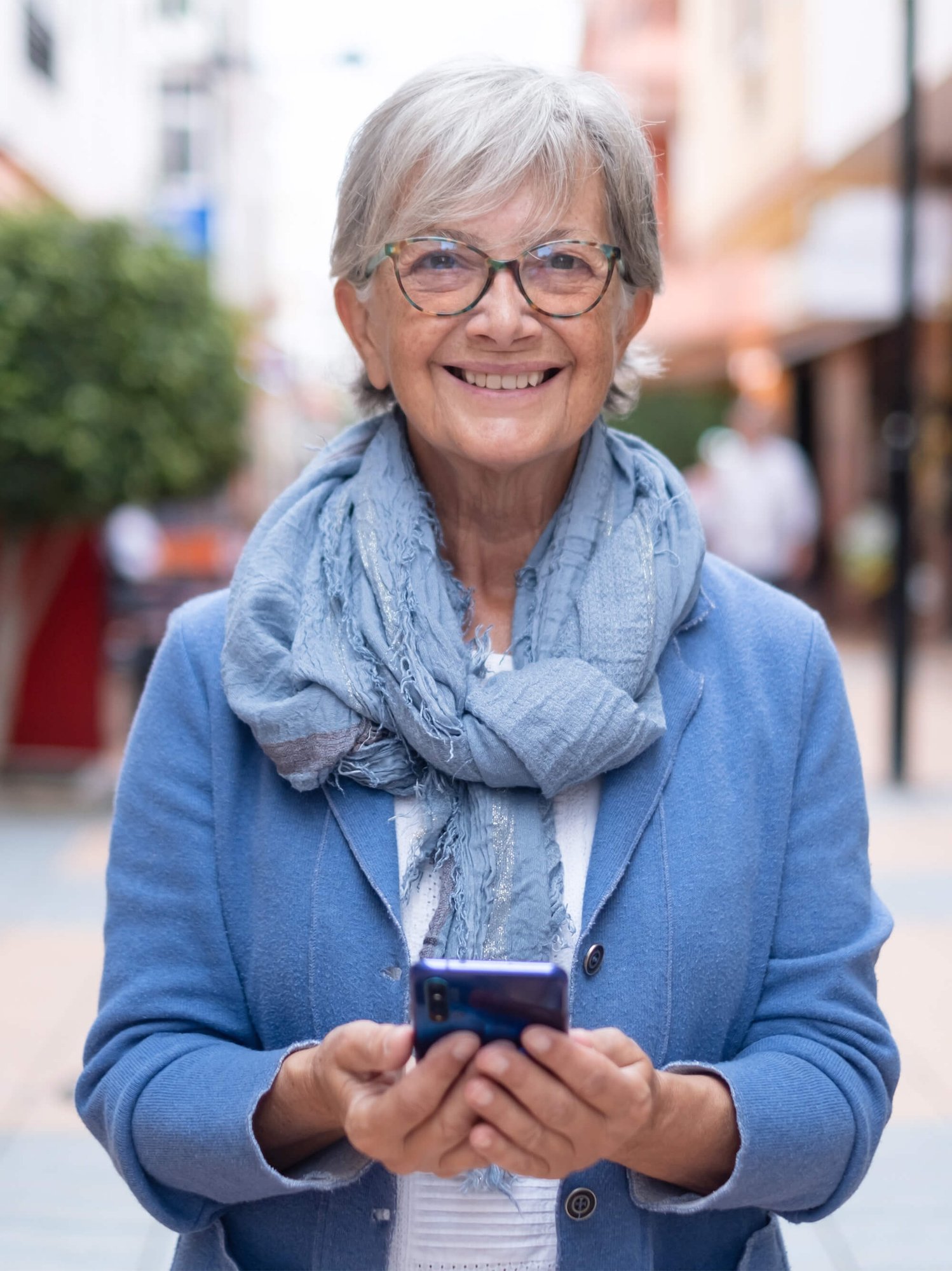 woman with gray hair walking in city street holding cellphone in hand